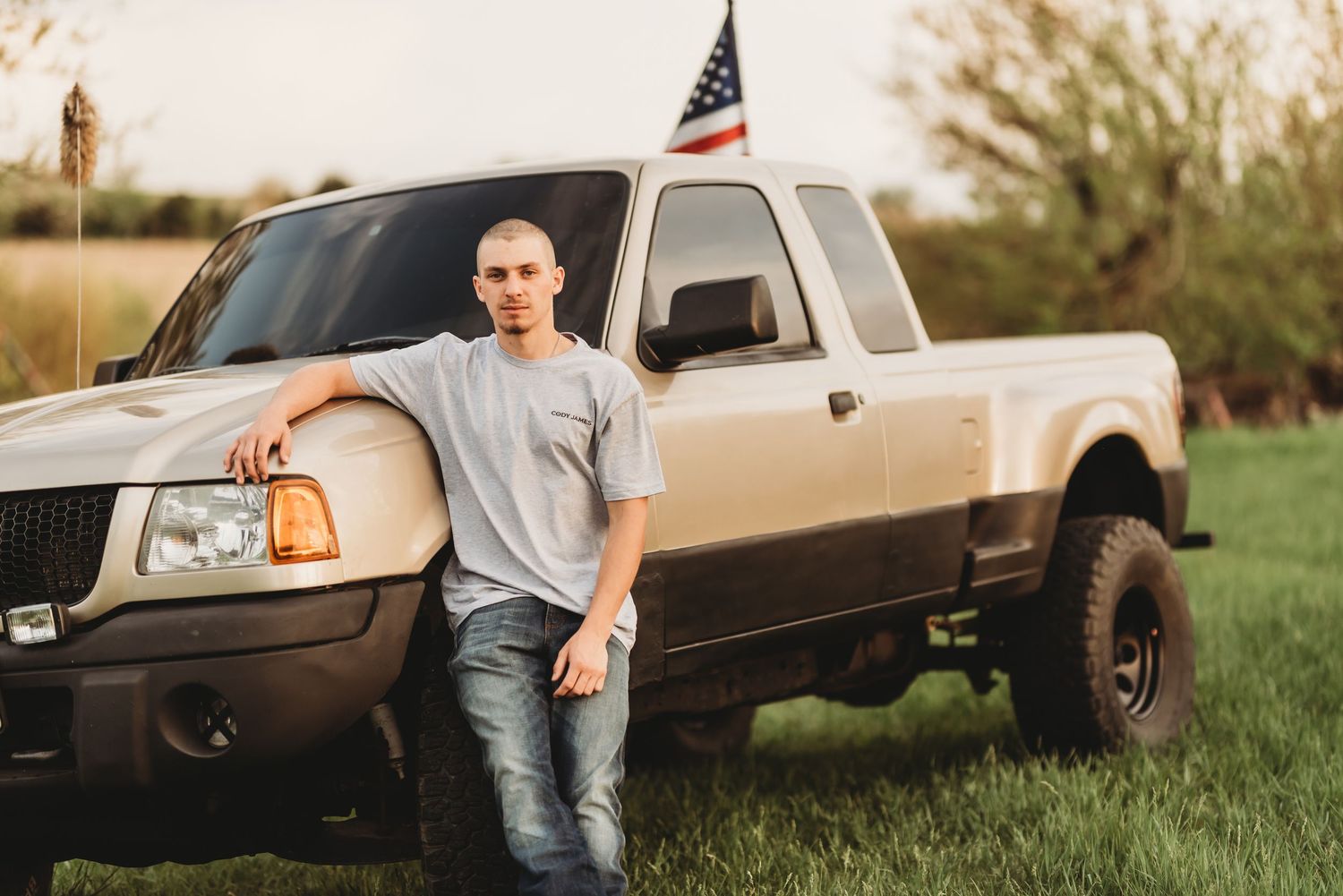 Person poses casually near pickup truck in grassy field at sunset.