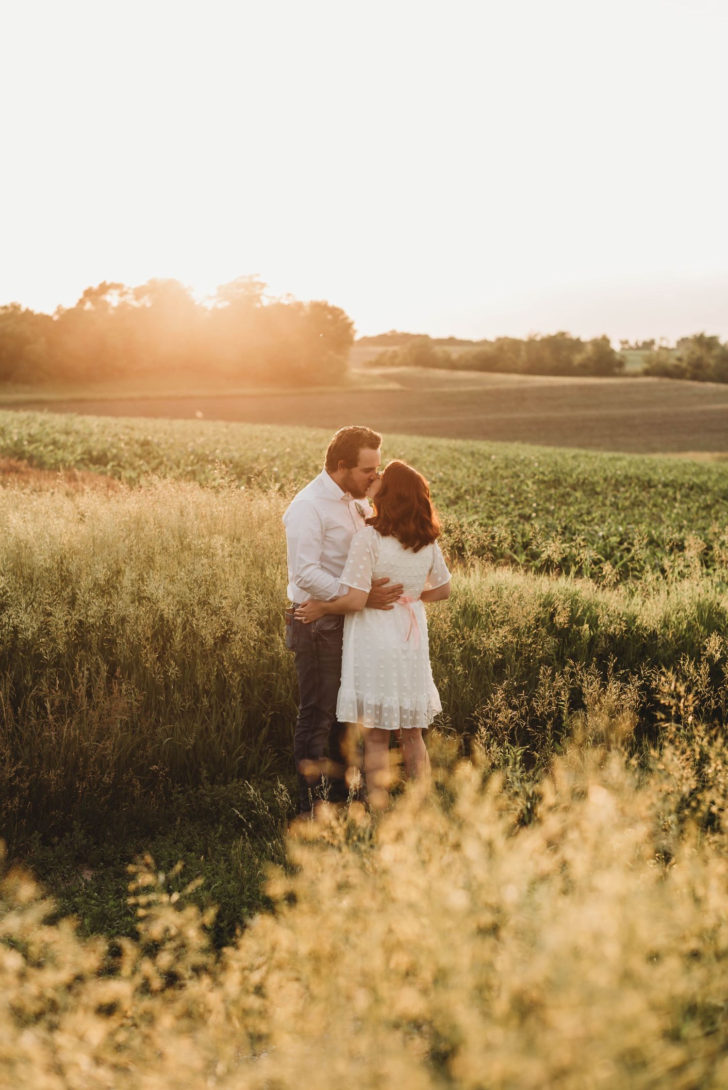 Couple embracing in golden field during sunset with warm backlight.