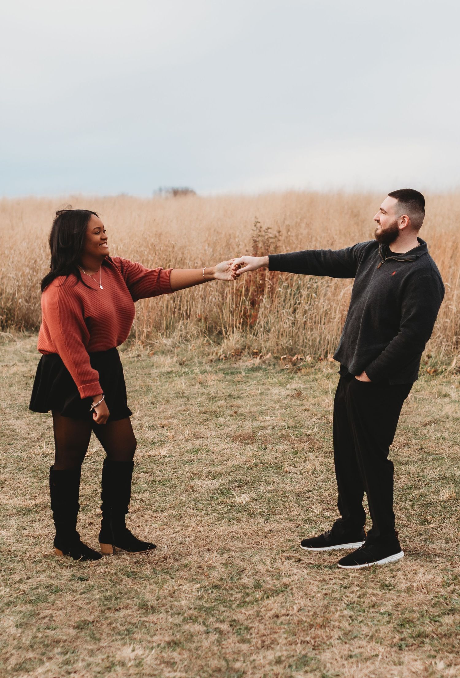 Two people reaching out to hold hands while standing in a golden wheat field.