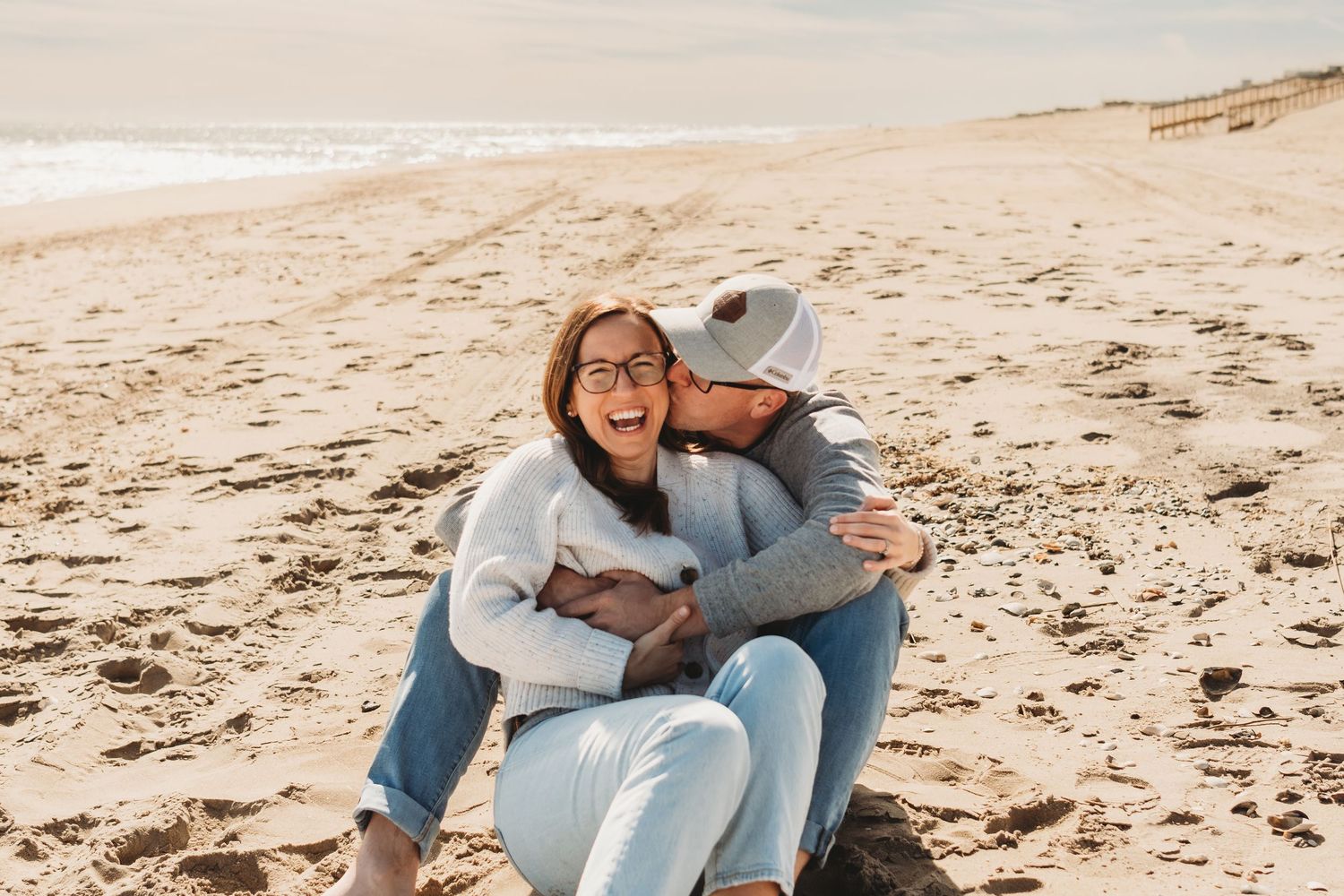 Couple laughing together while sitting on sandy beach shore.