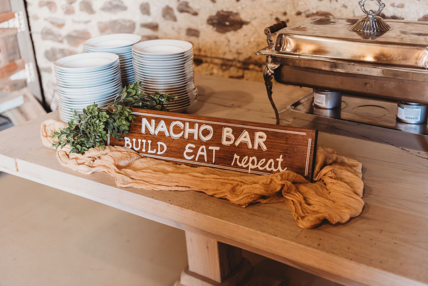 A rustic wedding reception setup featuring a nacho bar station with white plates and wooden decor elements.