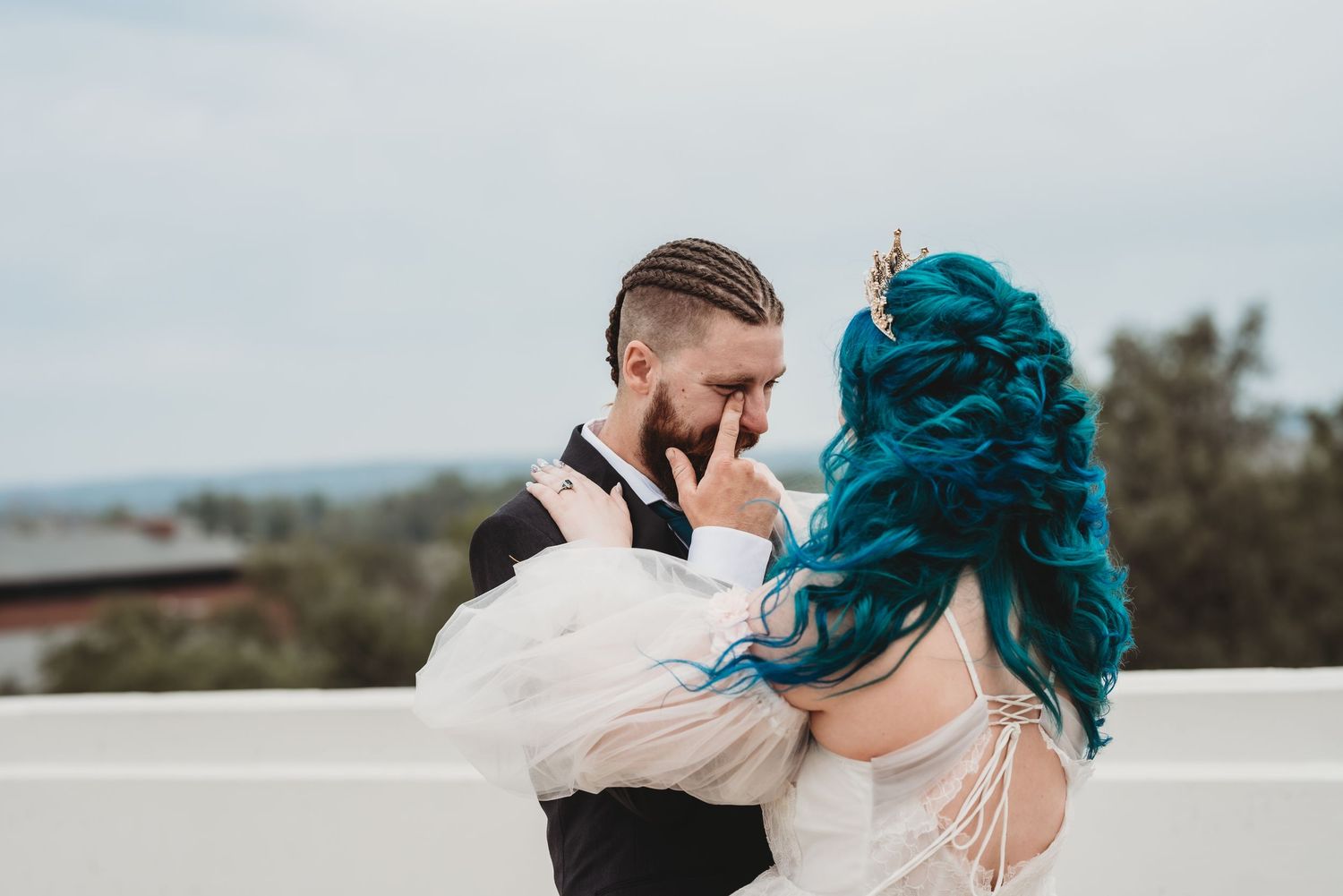 A romantic outdoor wedding moment with elegant attire and a striking turquoise hairstyle.