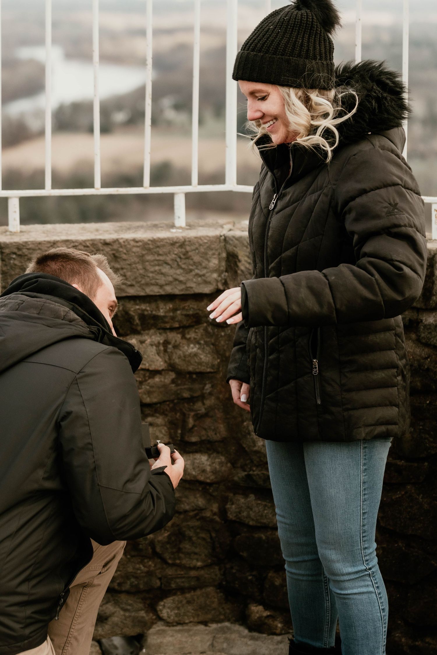 Winter proposal moment on stone wall overlook with person kneeling.