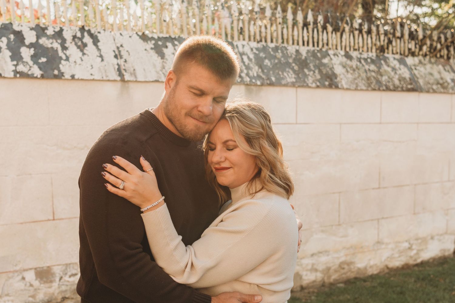 Couple embracing in warm neutral tones against textured wall background.