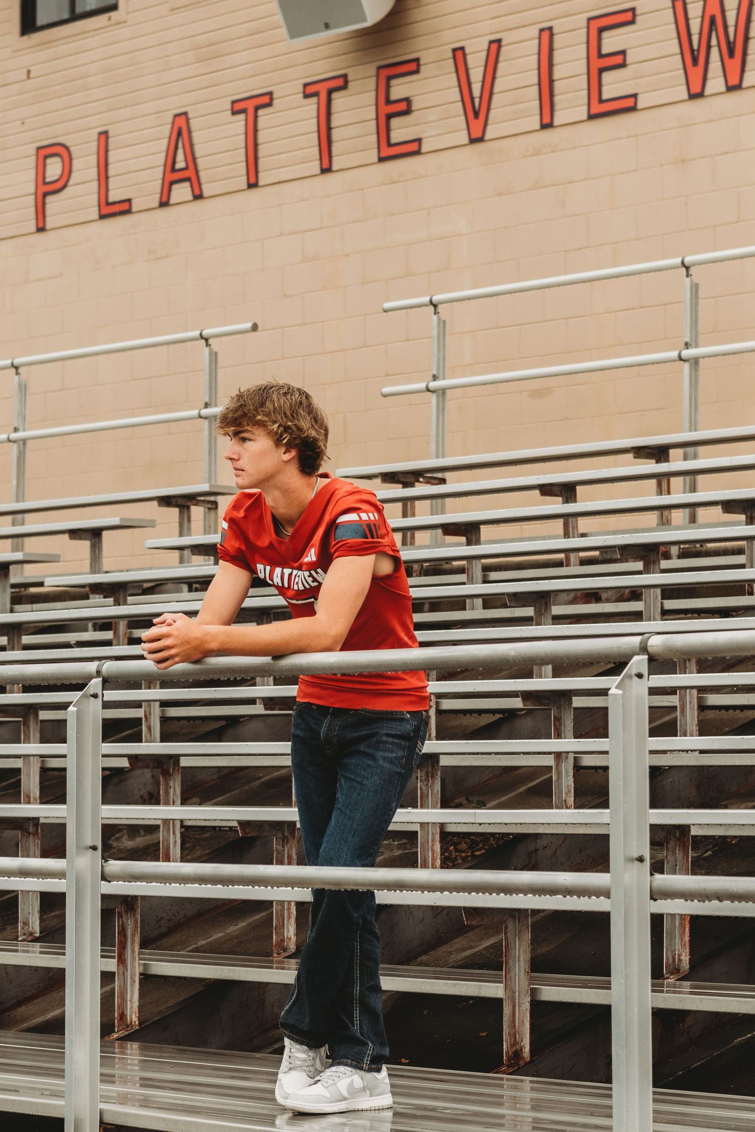 Student in football uniform standing on bleachers at Platteview stadium.