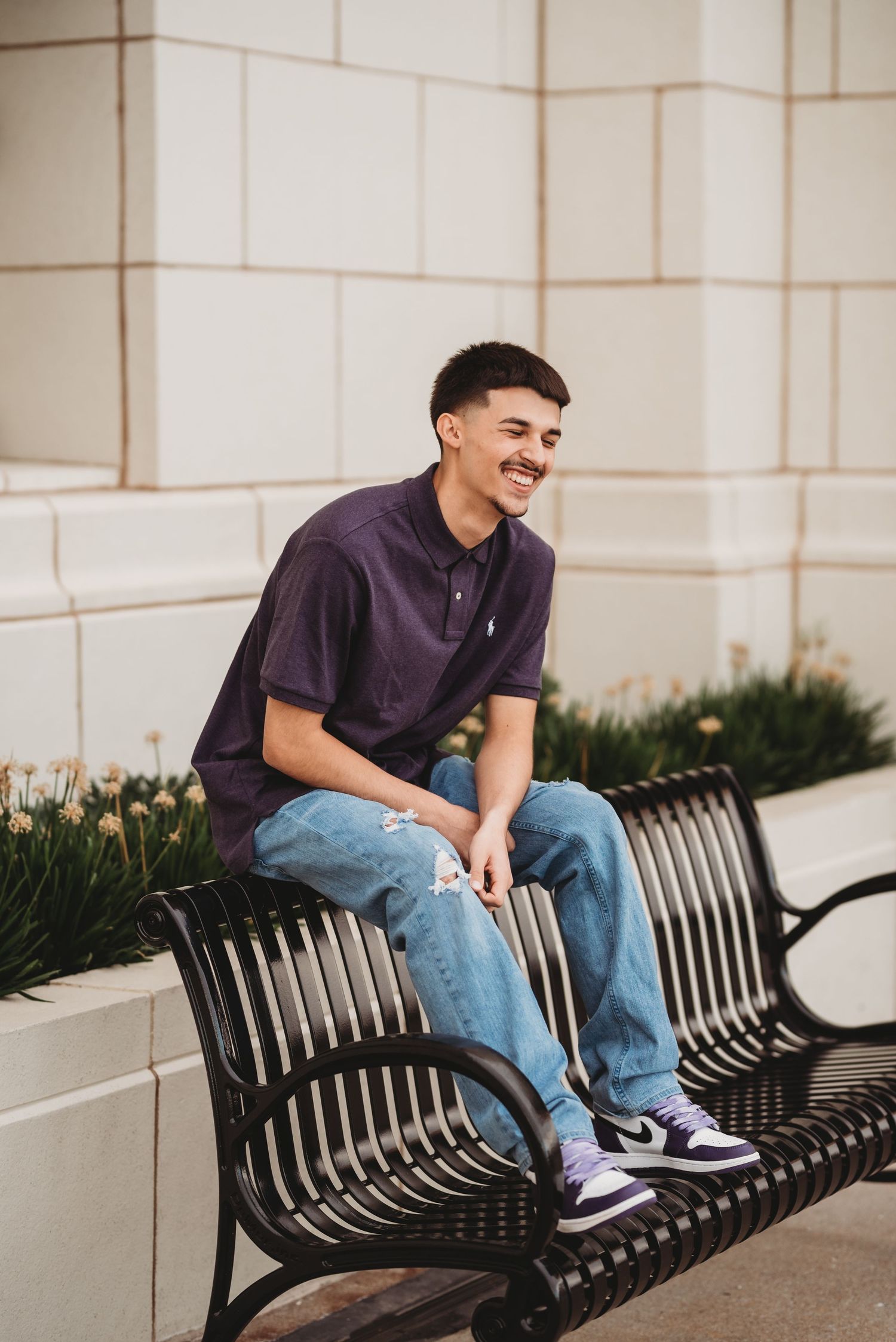 A person in a purple shirt sits relaxed on a black metal bench with a light colored wall behind them.