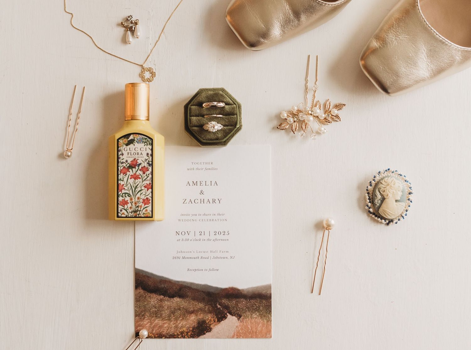 Wedding day details including jewelry, candles and stationery arranged on white surface.