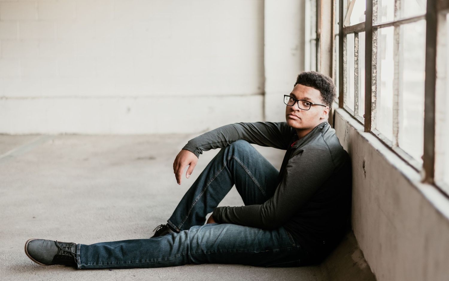 A person wearing dark clothing lies on their side along a white wall with windows.
