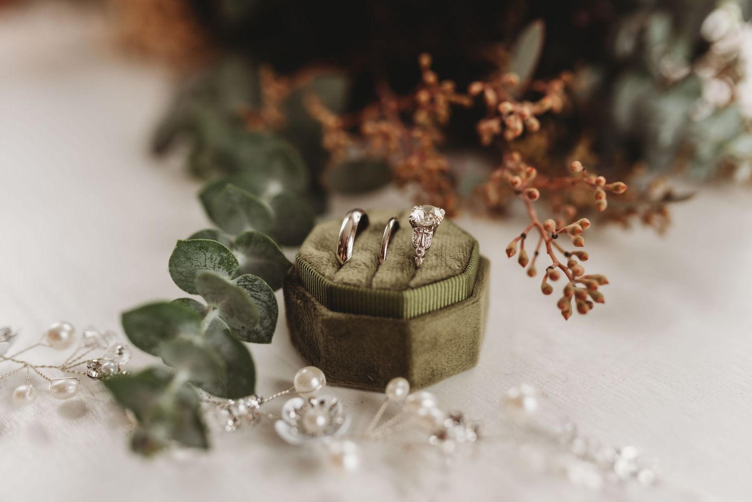 Wedding rings and delicate floral decorations arranged on a white surface.