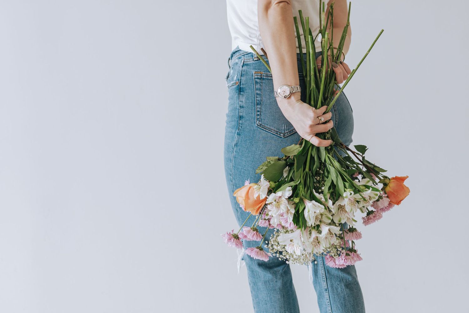 Person in blue jeans holding fresh cut flowers against white background.