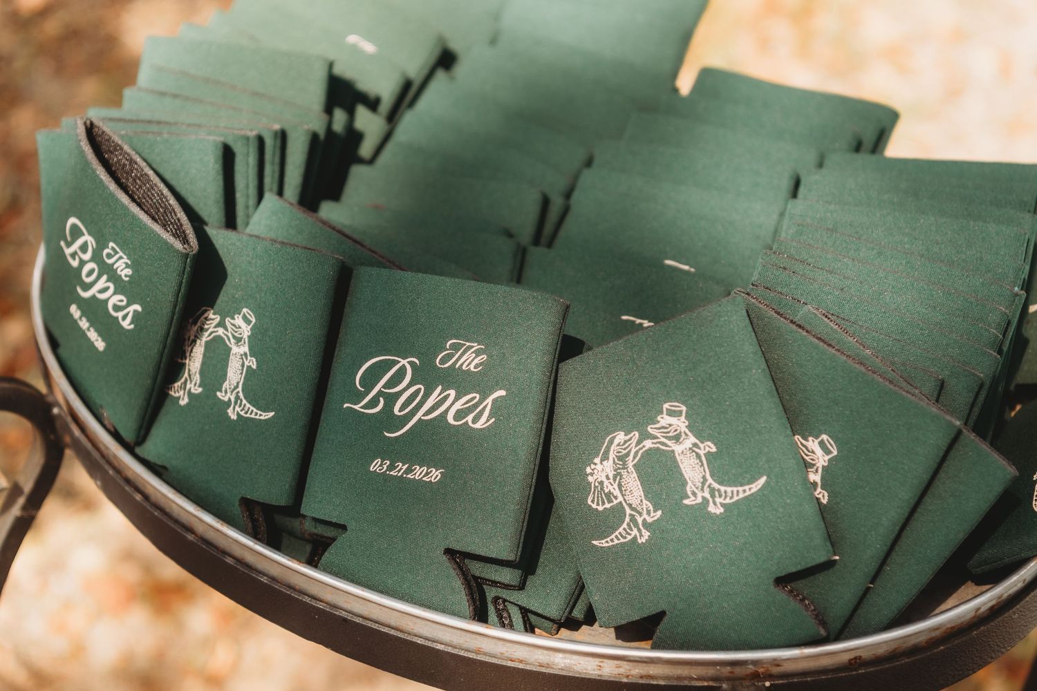 Green custom wedding koozies printed with The Popes name and date, displayed in a decorative tray as party favors.