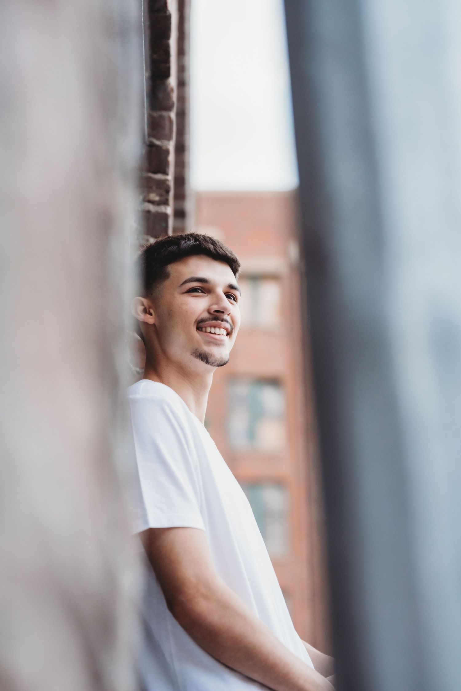 A person in white t-shirt smiles while posing against a blurred architectural background.