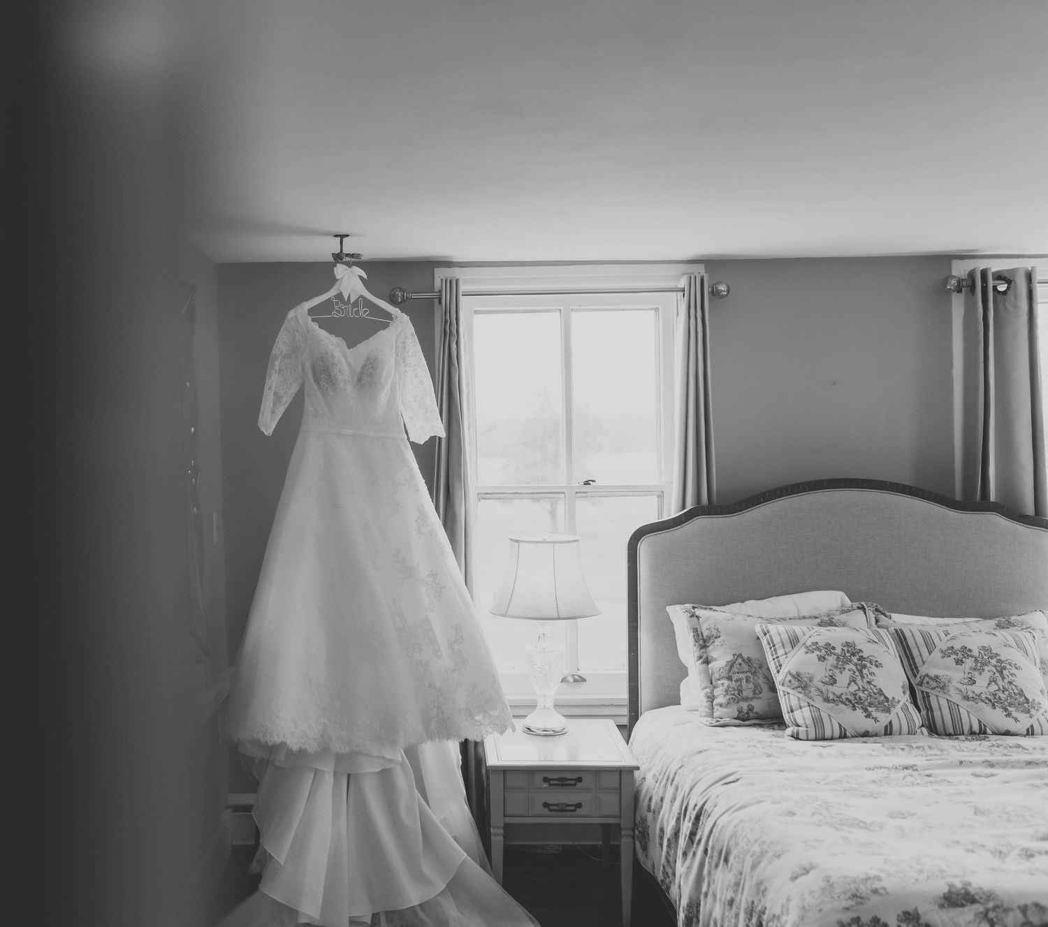 Black and white photos of a wedding dress hanging in a bedroom setting.
