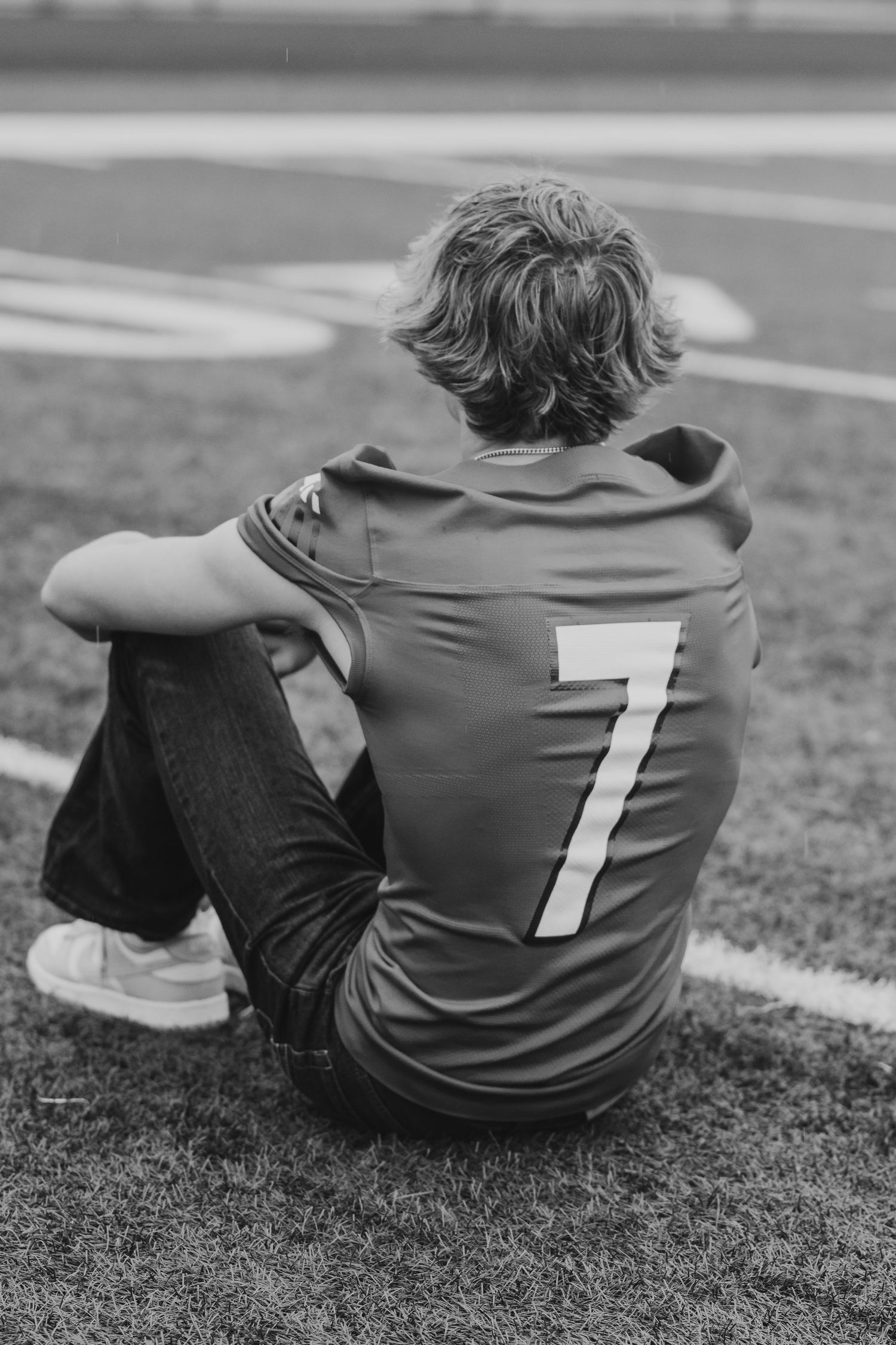 Back view of athlete wearing jersey number 7 sitting on sports field.