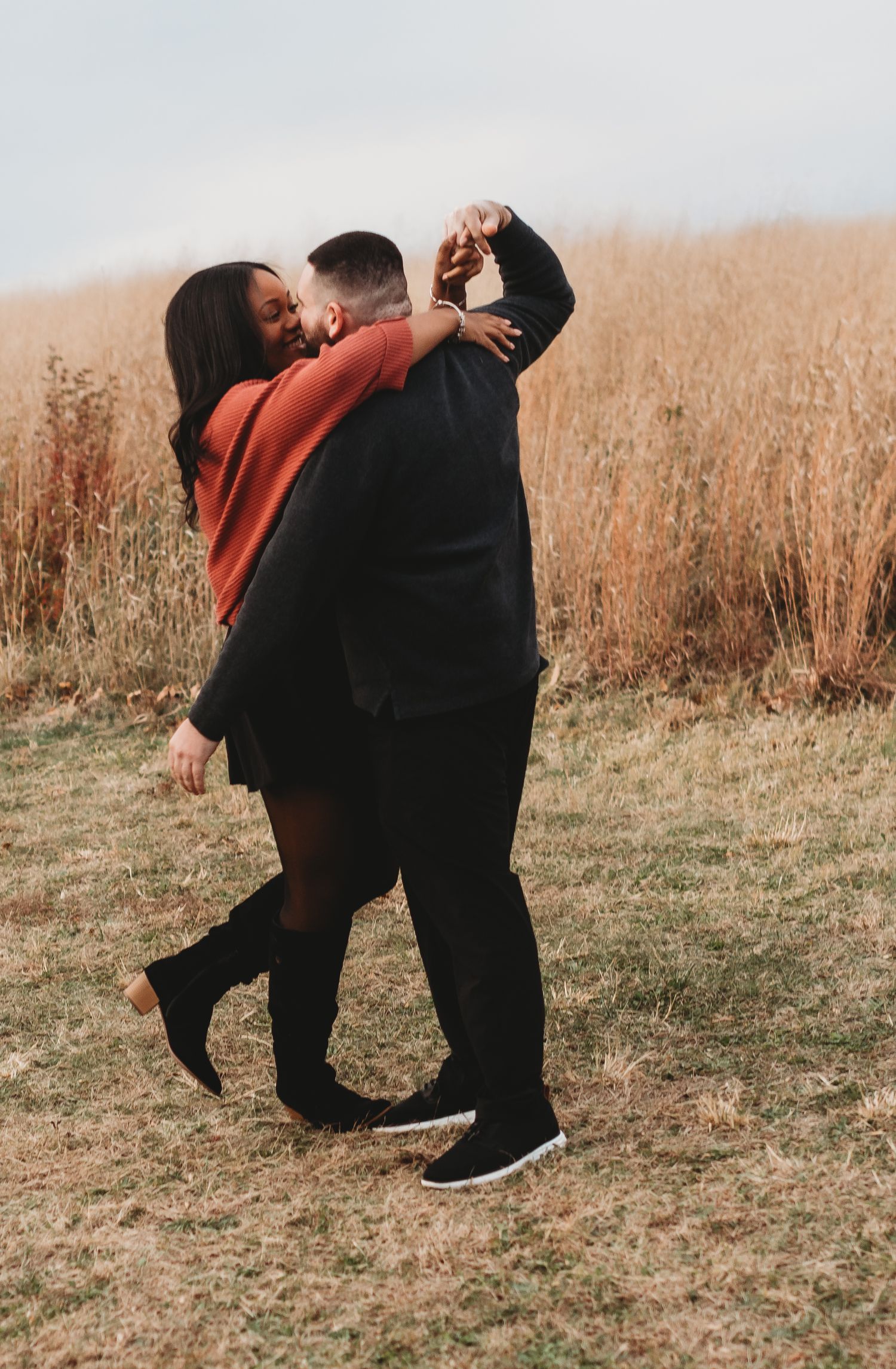 Couple in black and orange outfits sharing playful moments in a fall field.