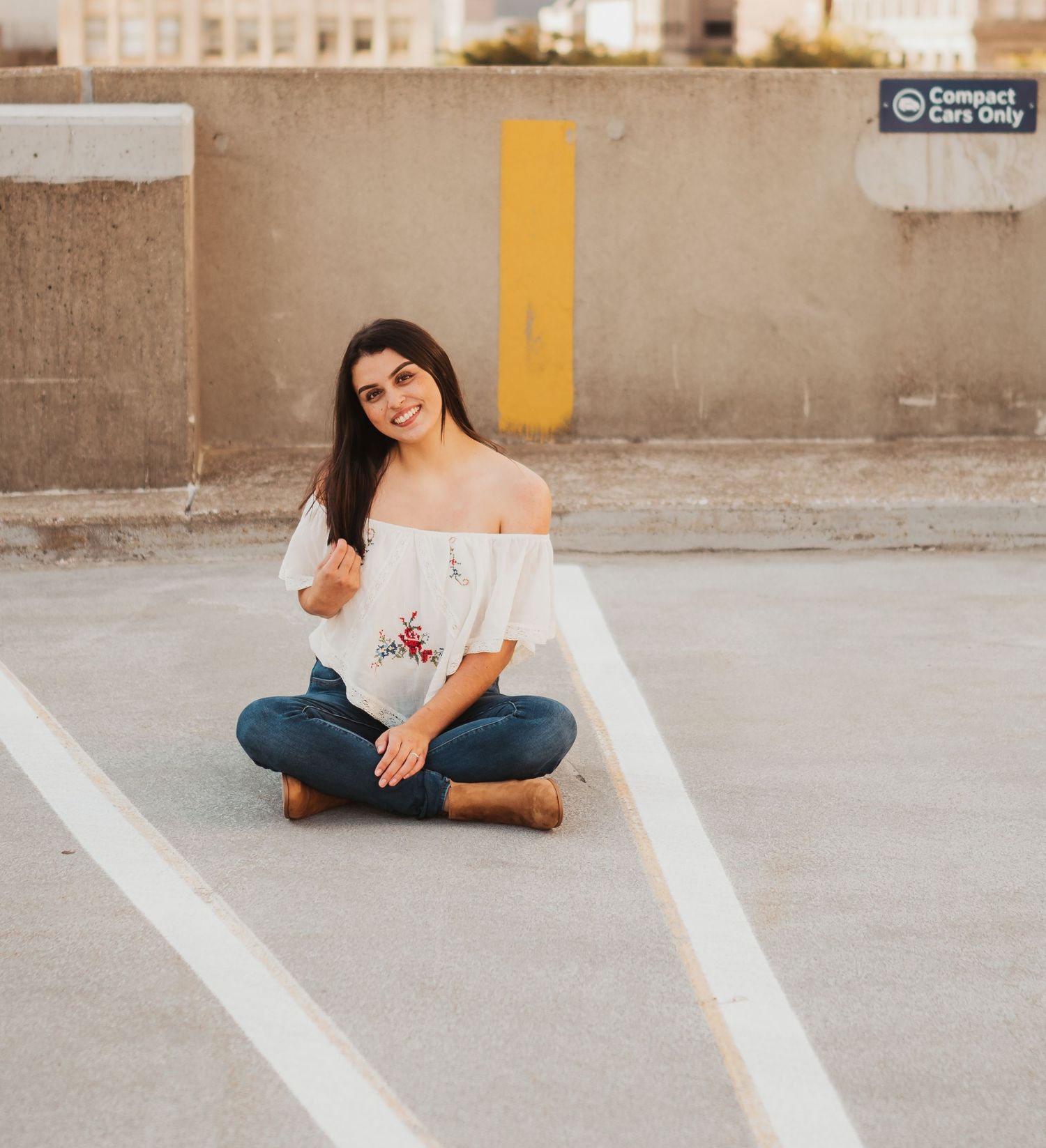 A person in blue jeans and white top sits on a concrete surface with painted white lines.