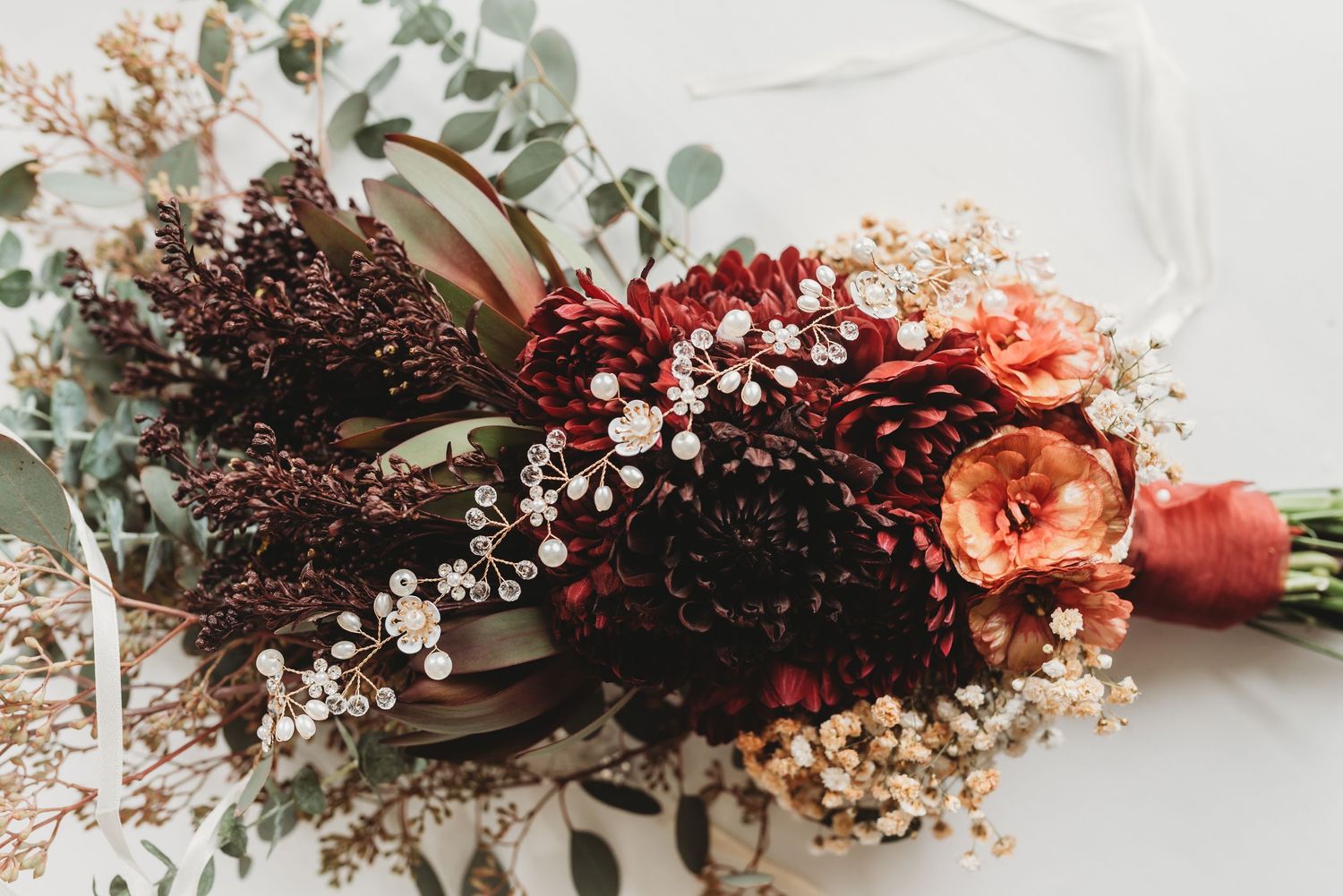 Dried floral arrangement with baby's breath and burgundy flowers on white surface.