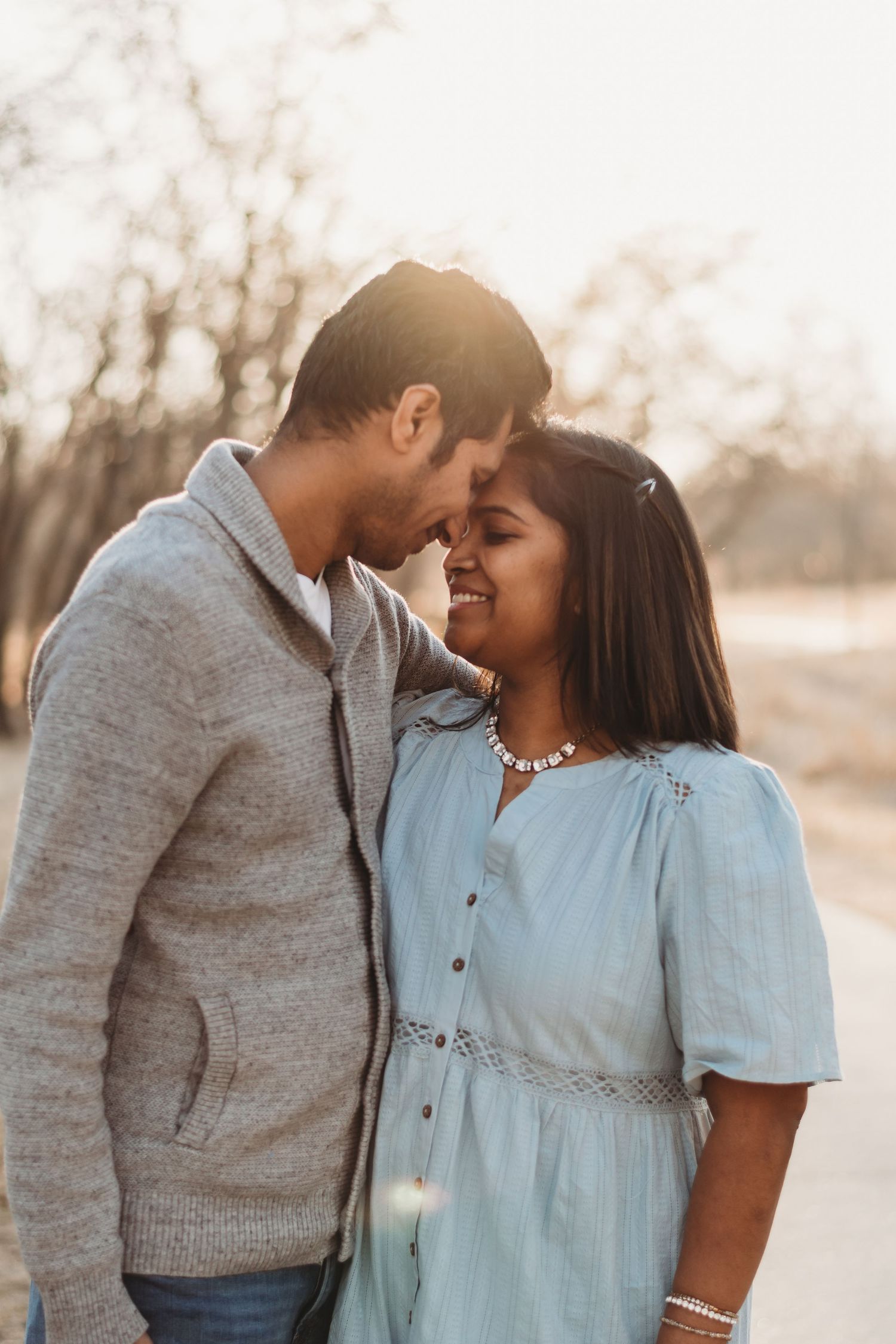 A couple shares an intimate moment in soft sunset lighting wearing casual attire.