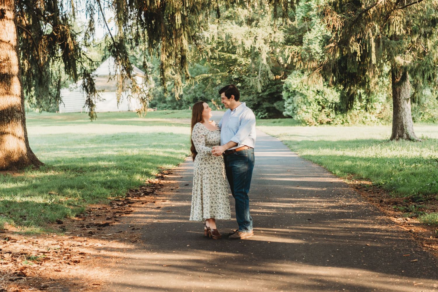 Couple sharing a romantic moment on a tree-lined path in a lush green park during golden hour.