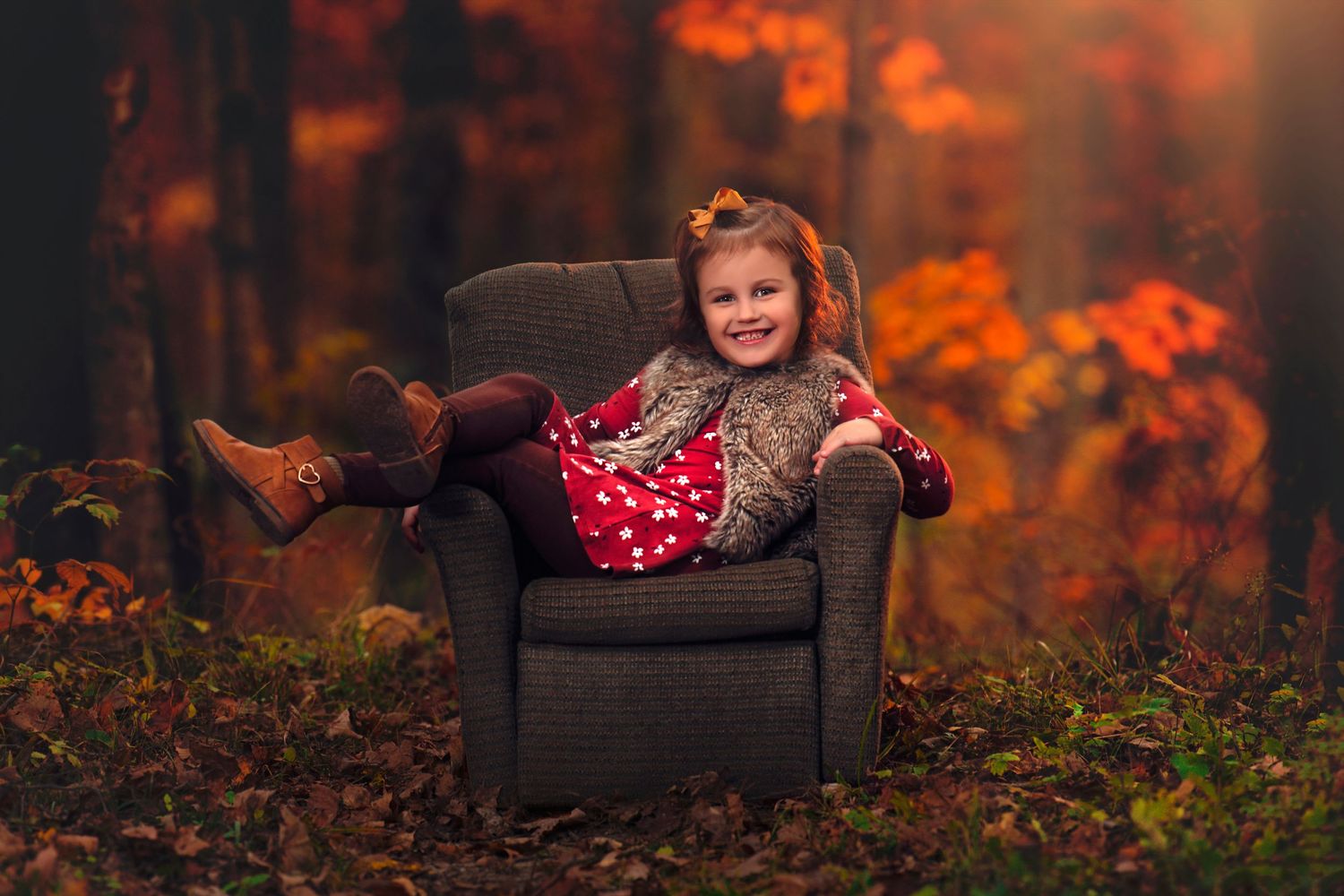 Young girl in red polka dot dress relaxes in gray armchair surrounded by vibrant autumn forest.