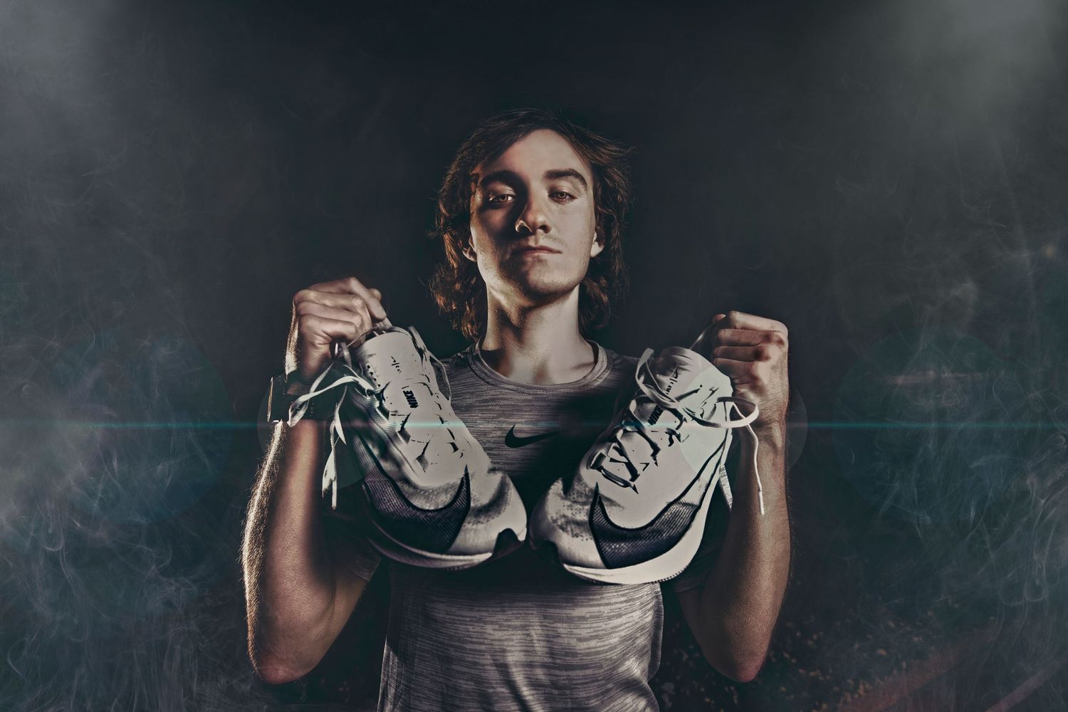 Young male athlete holding Nike sneakers with eyes closed against dark smoky background.
