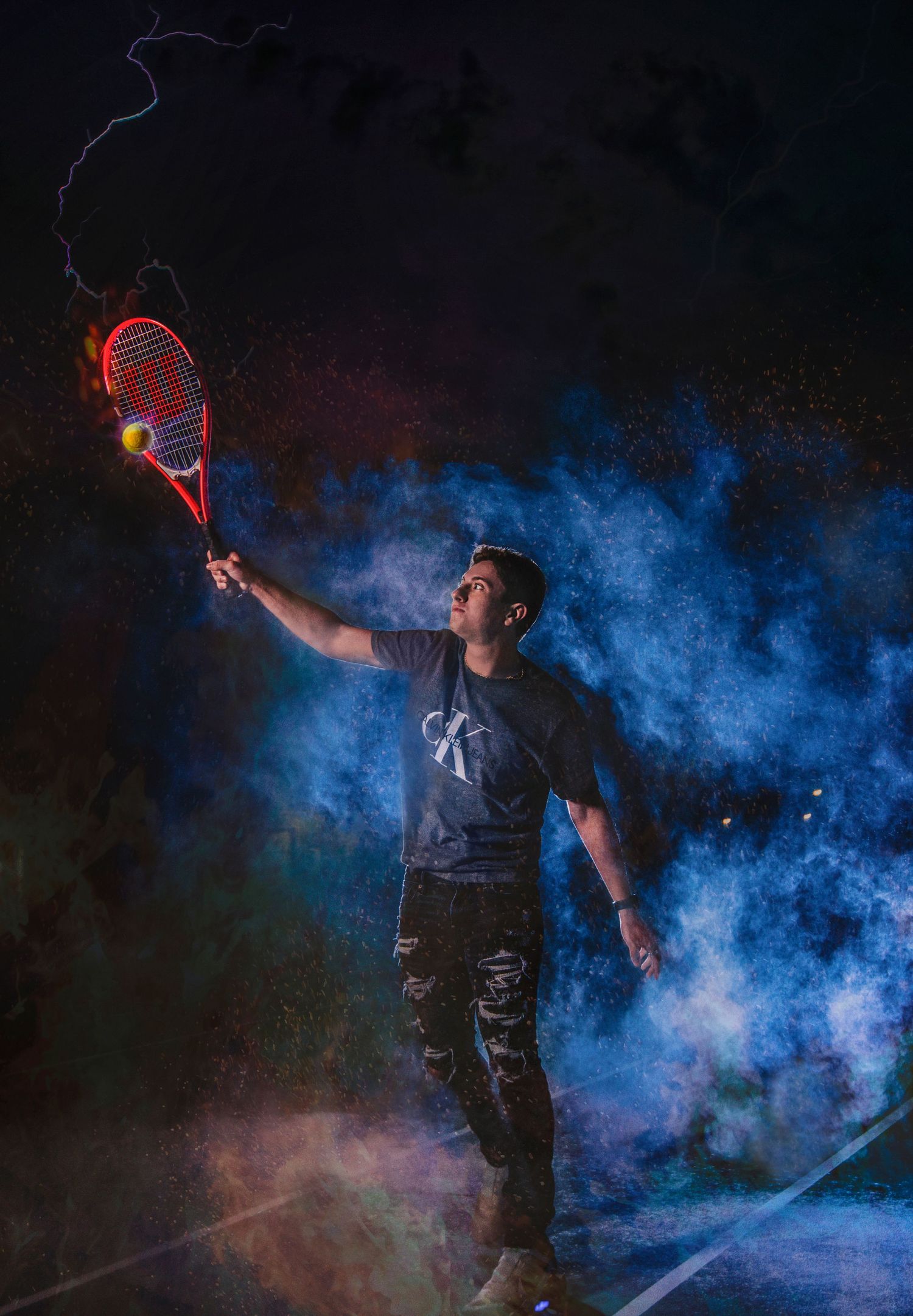 Man holding a tennis racket with lightning bolt effect surrounded by colorful smoke at night.
