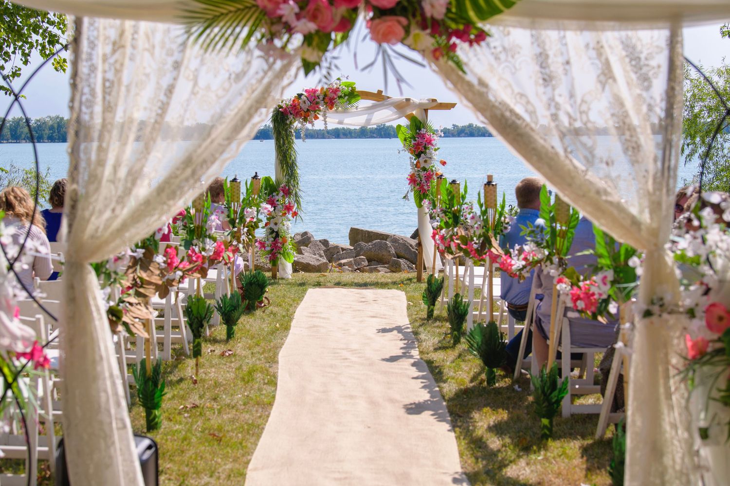 Elegant outdoor wedding ceremony aisle decorated with pink flowers and white draping overlooking a waterfront.