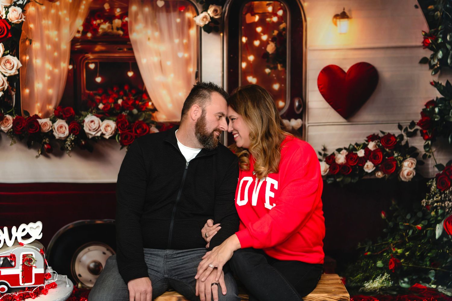 Romantic couple shares tender moment surrounded by red roses and hearts in Valentine's Day themed setting.