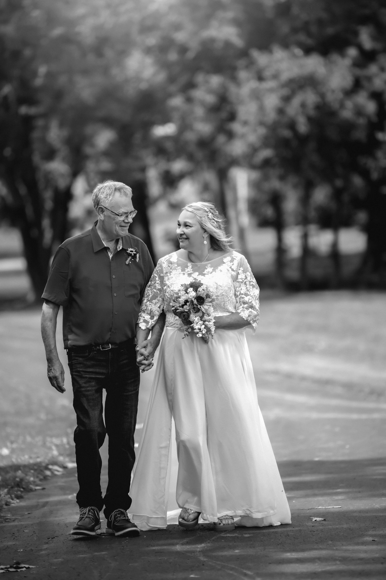 Black and white photo of smiling bride holding bouquet walking with older man outdoors.