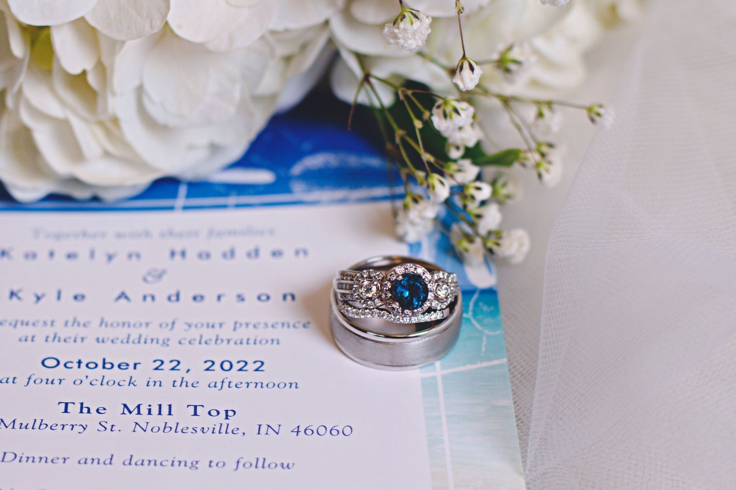 Blue sapphire engagement ring and wedding band resting on a wedding invitation dated October 22, 2022.