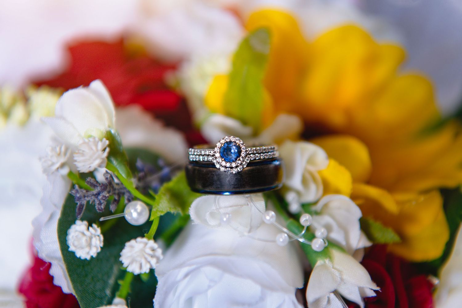 Silver engagement ring with blue sapphire center stone resting on a vibrant colorful bridal bouquet.