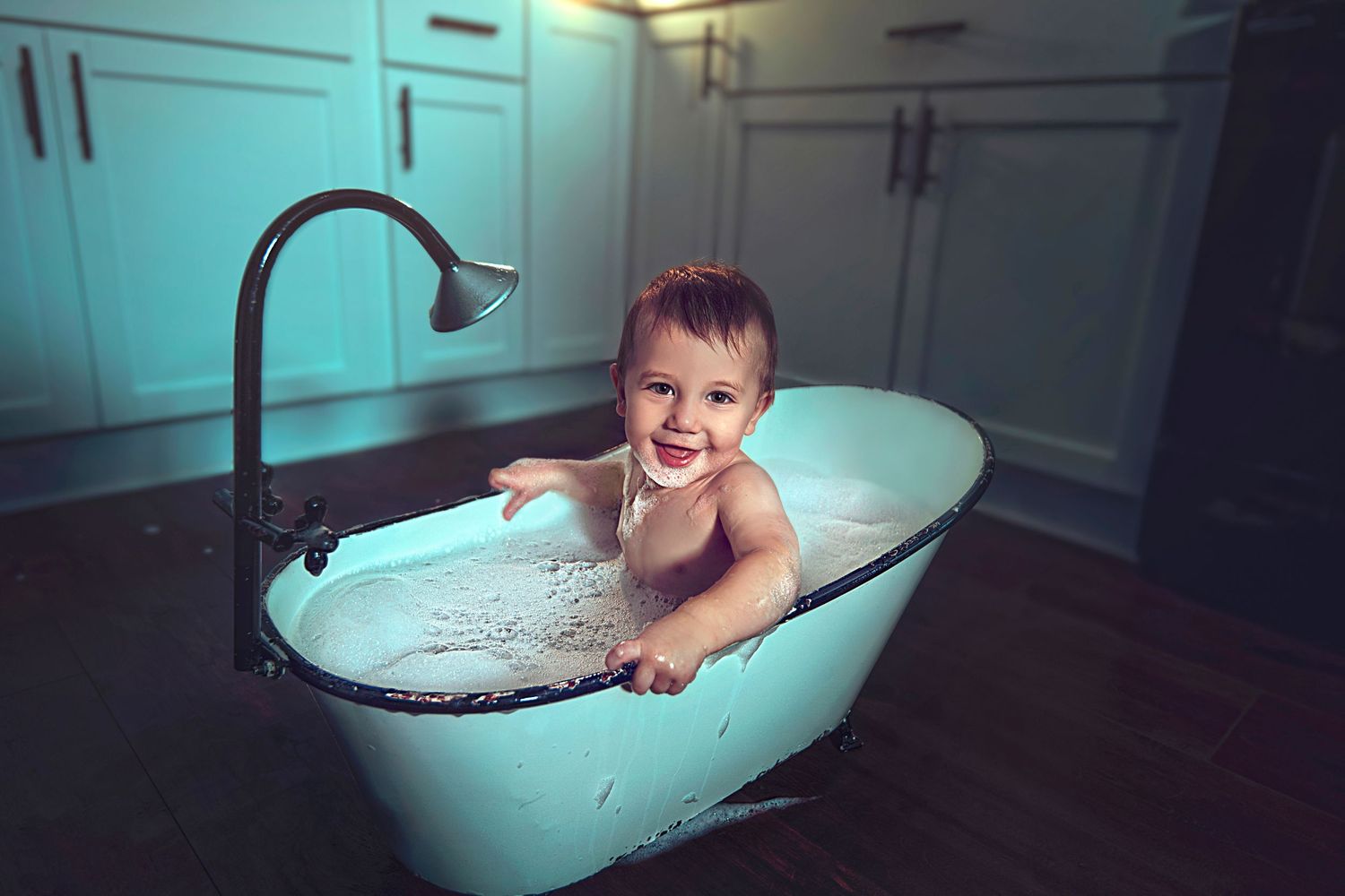Happy baby smiling in a vintage mint green clawfoot bathtub indoors.