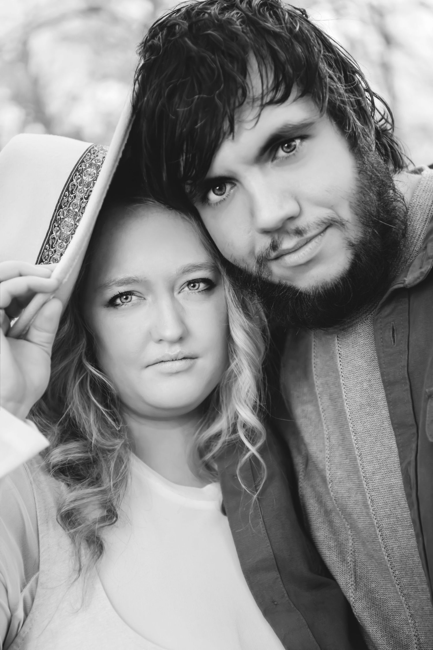 Black and white portrait of a young couple, woman wearing a white hat leaning against bearded man.