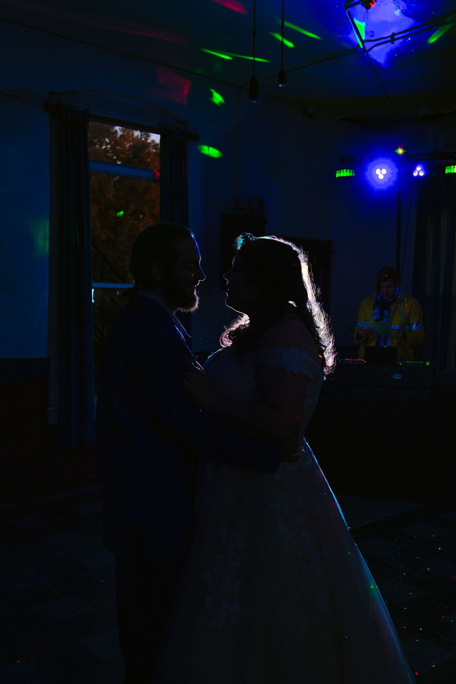 Silhouette of bride and groom sharing first dance under colorful disco lights in a darkened reception venue.
