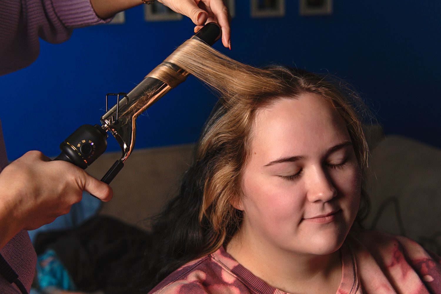 Young woman with eyes closed getting hair curled with a curling iron during wedding preparation.
