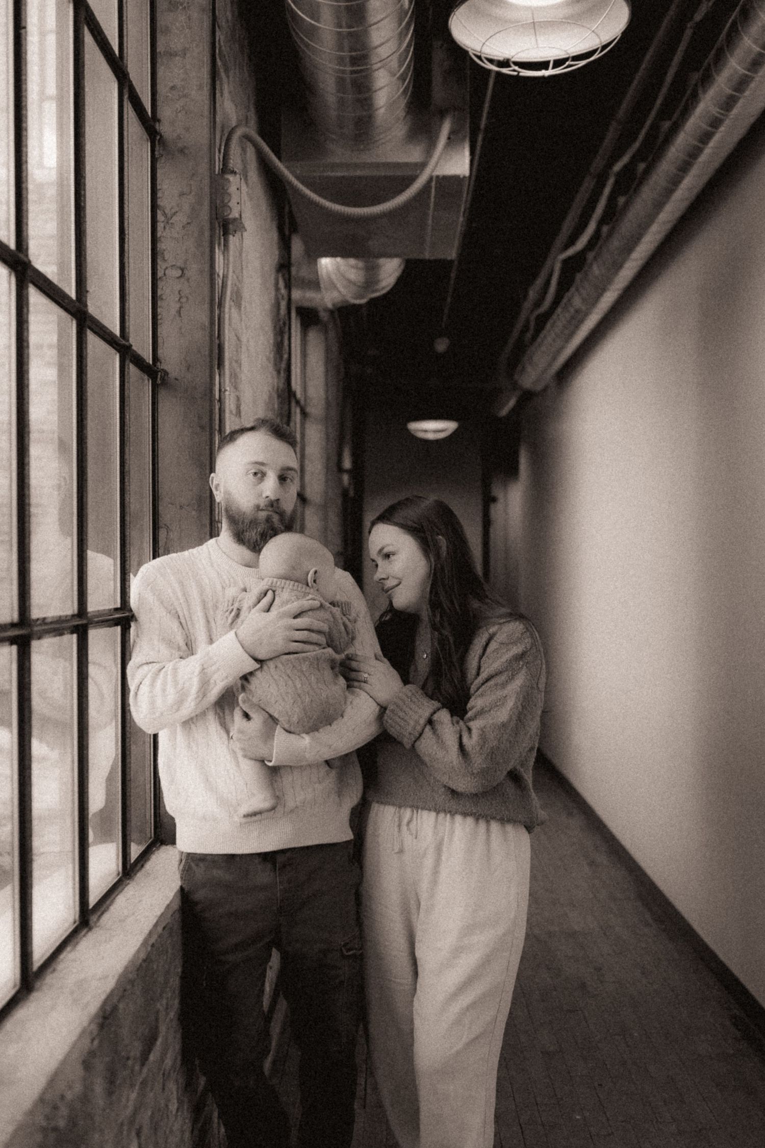 A sequence of black and white photographs showing tender embraces in an industrial hallway setting.