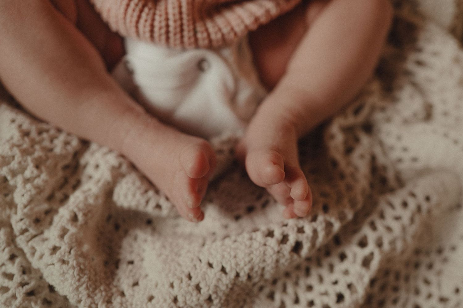 Close-up details of tiny baby hands grasping and touching a textured knit blanket.