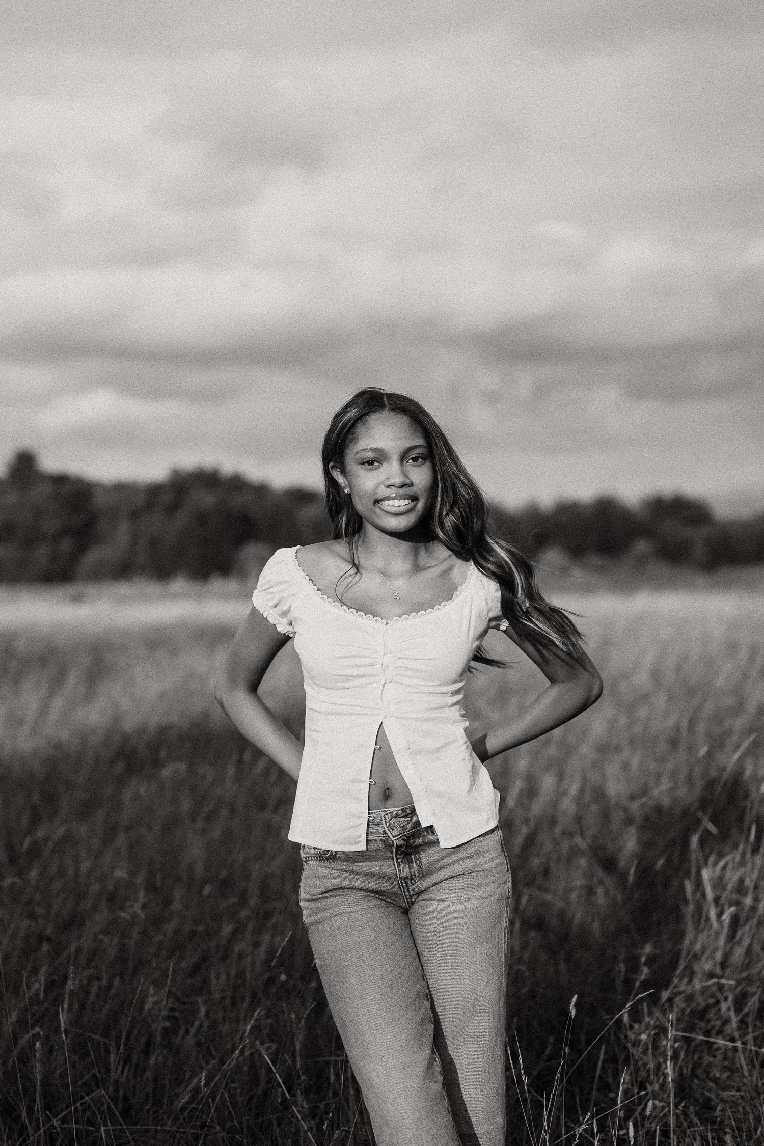 Black and white portrait of smiling woman in white top standing in field.