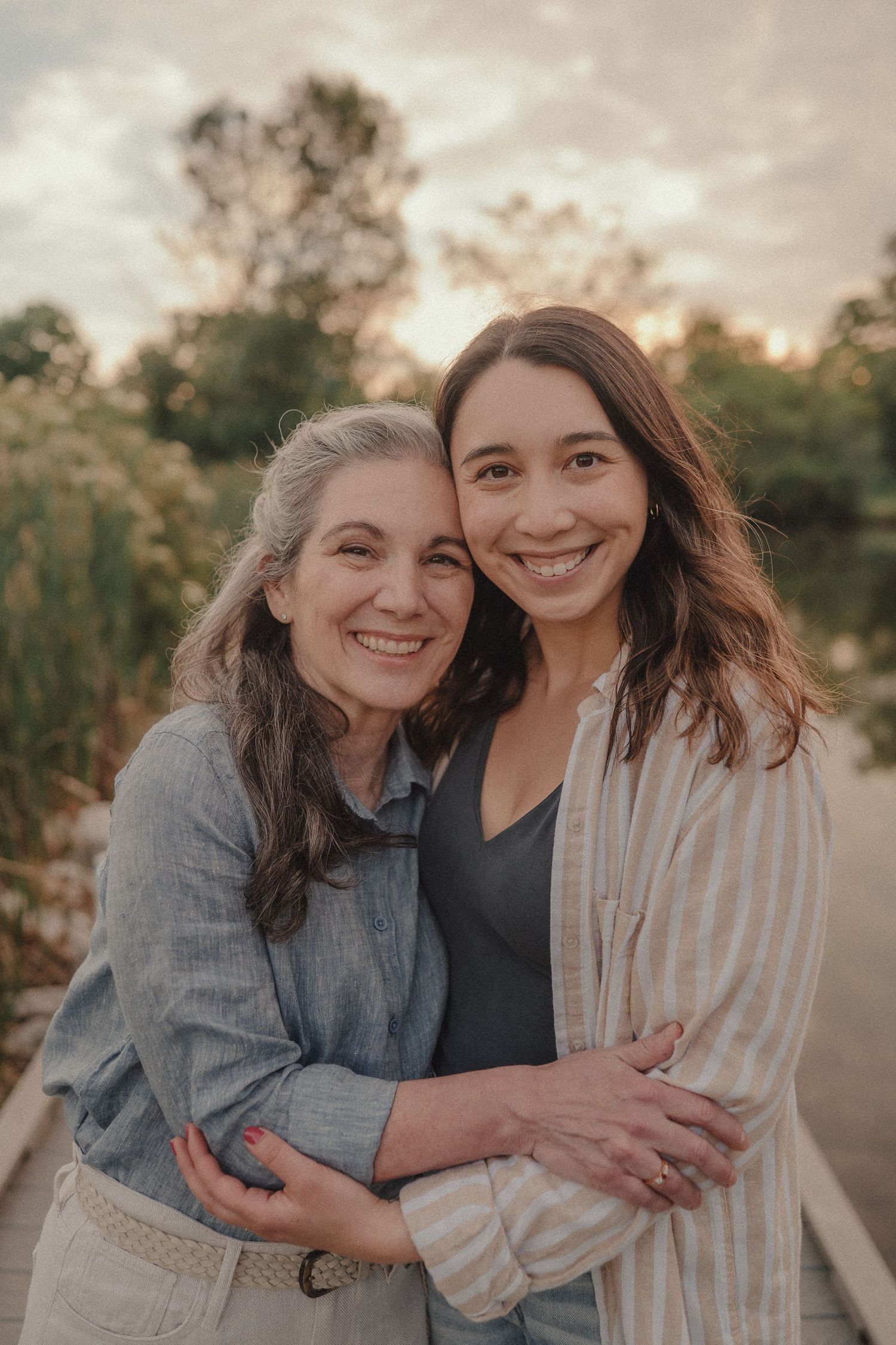 Two smiling women embracing warmly on outdoor dock with soft sunset bokeh background.