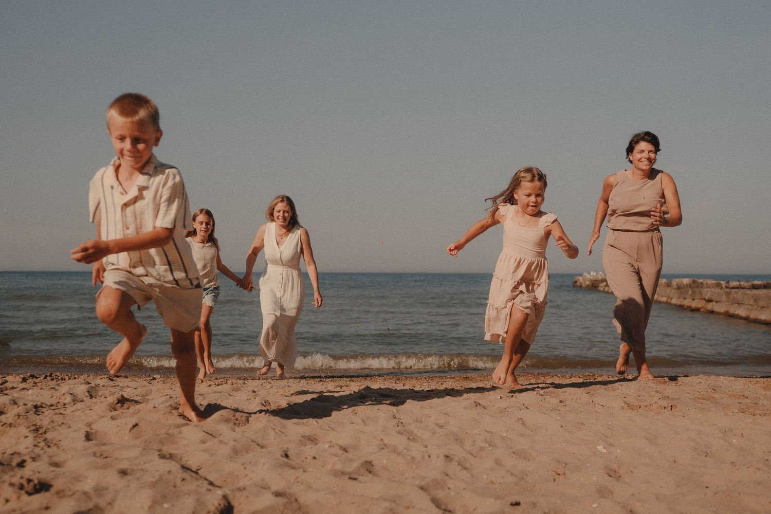 Joyful family with two women and three children running and playing together on a sunny sandy beach.