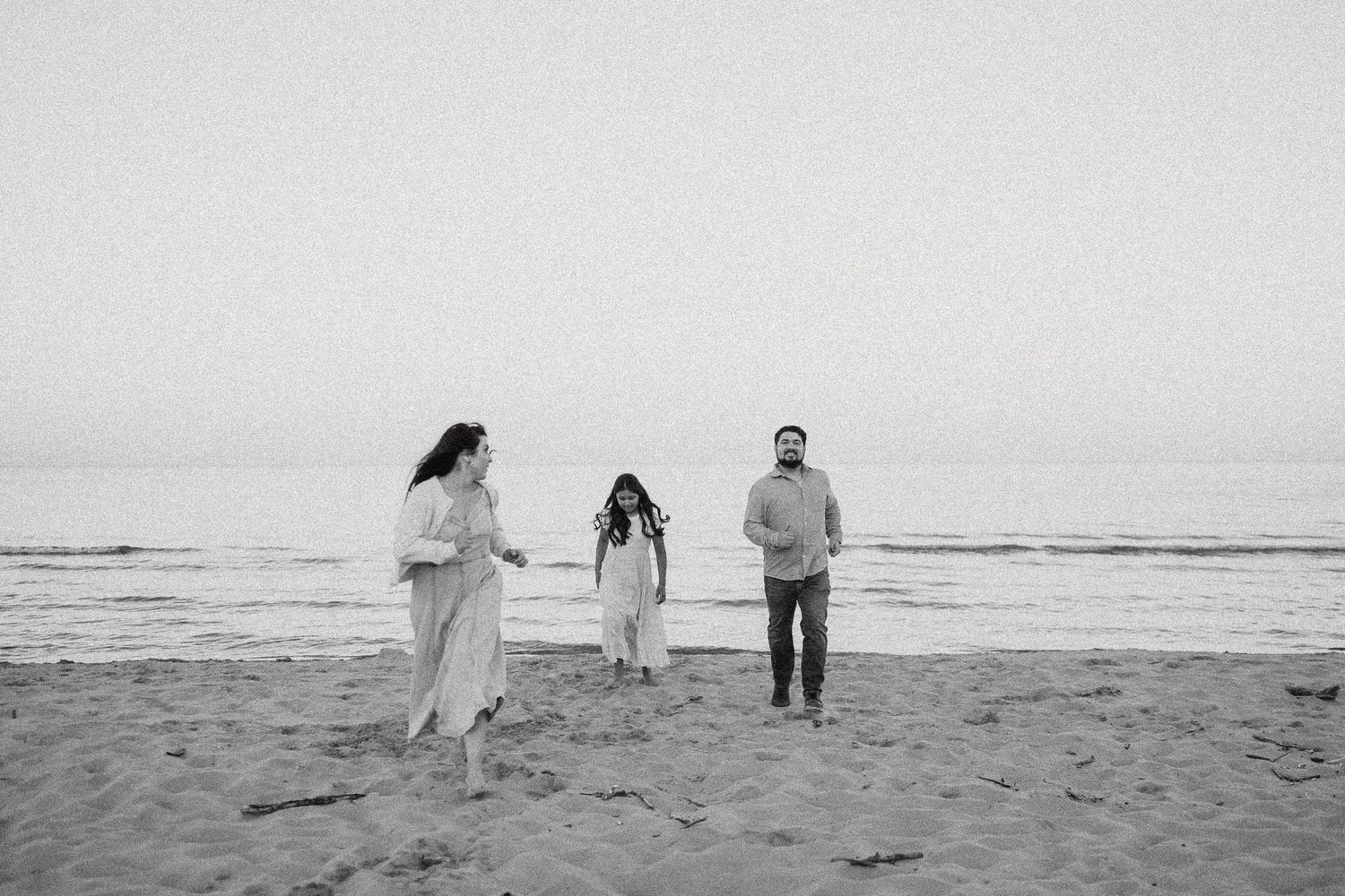 Black and white photo of a family of three walking on a sandy beach with ocean waves in the background.