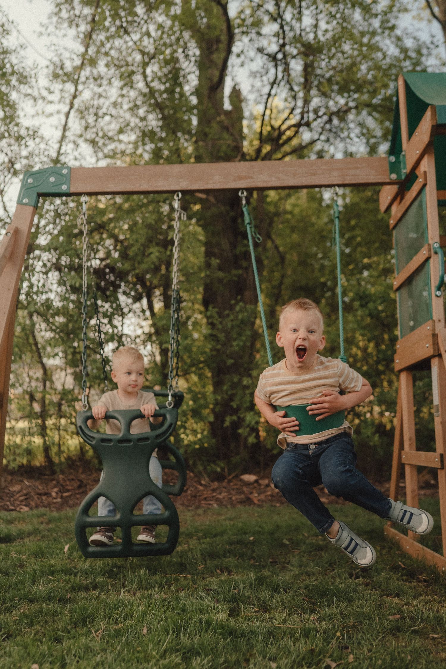 Two young brothers laugh and play on backyard swings on a bright spring day.