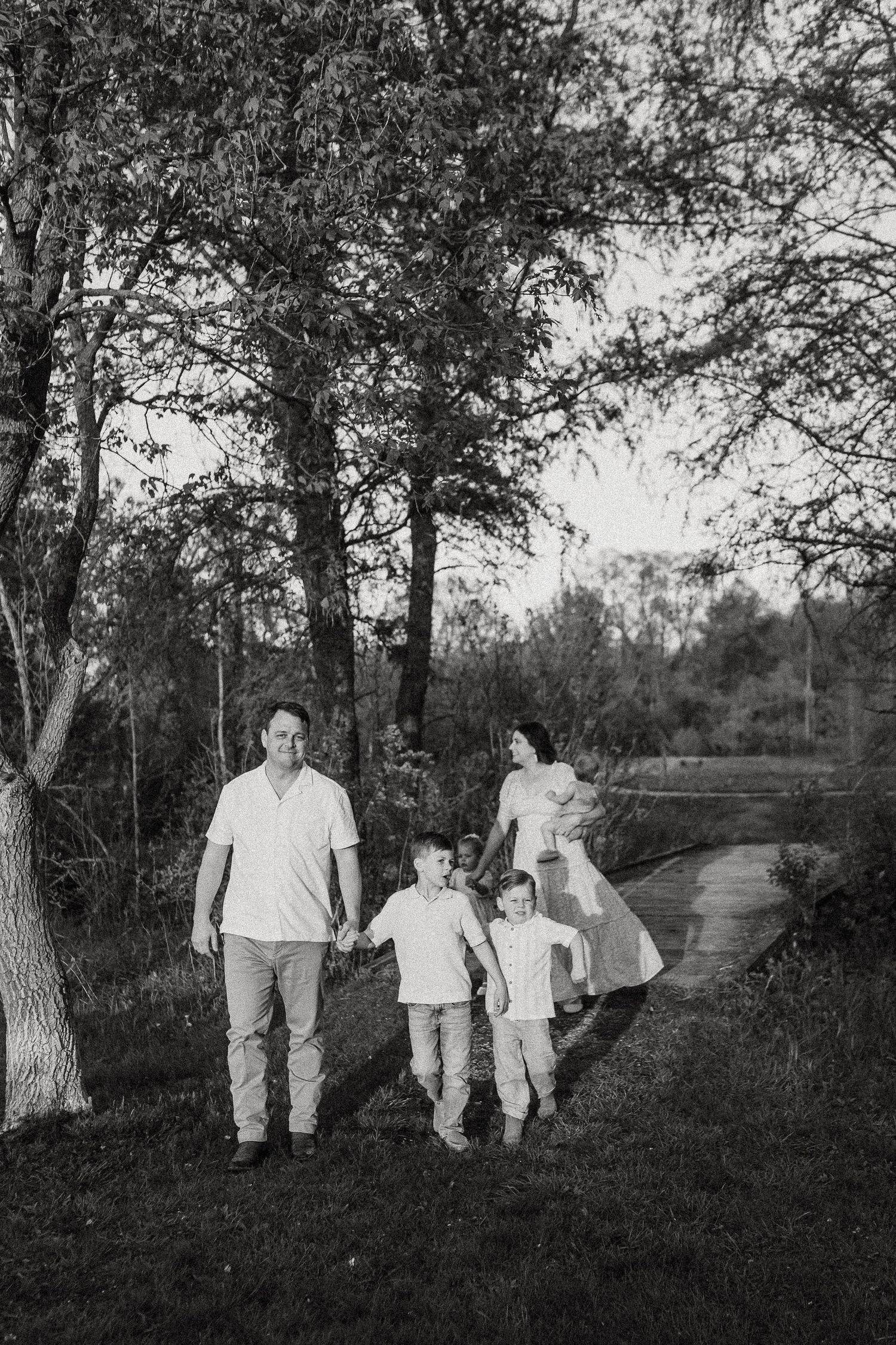 Black and white photo of family walking hand in hand along tree-lined path at dusk.