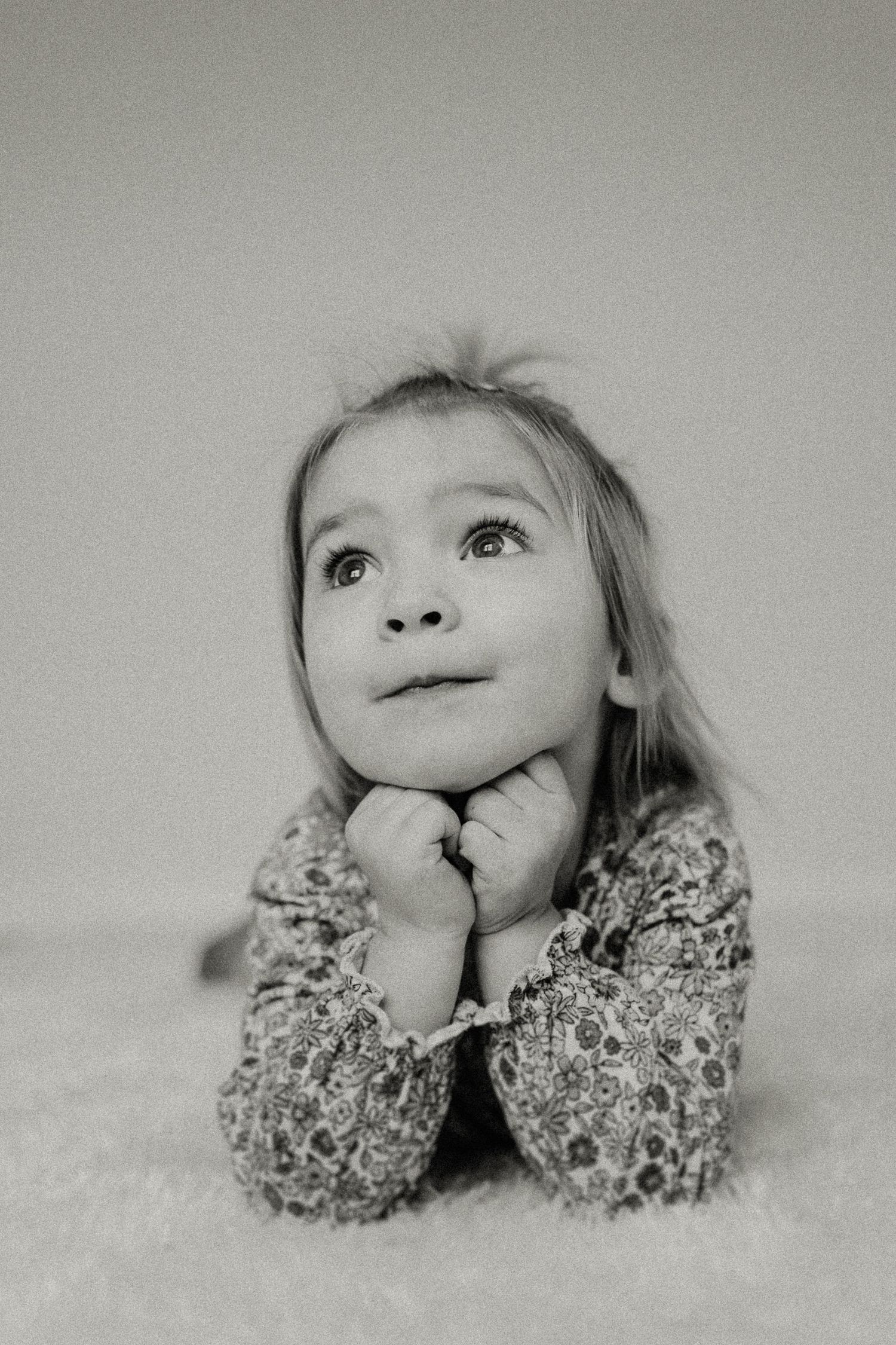 Black and white portrait of a child in a floral sweater with a dreamy expression.