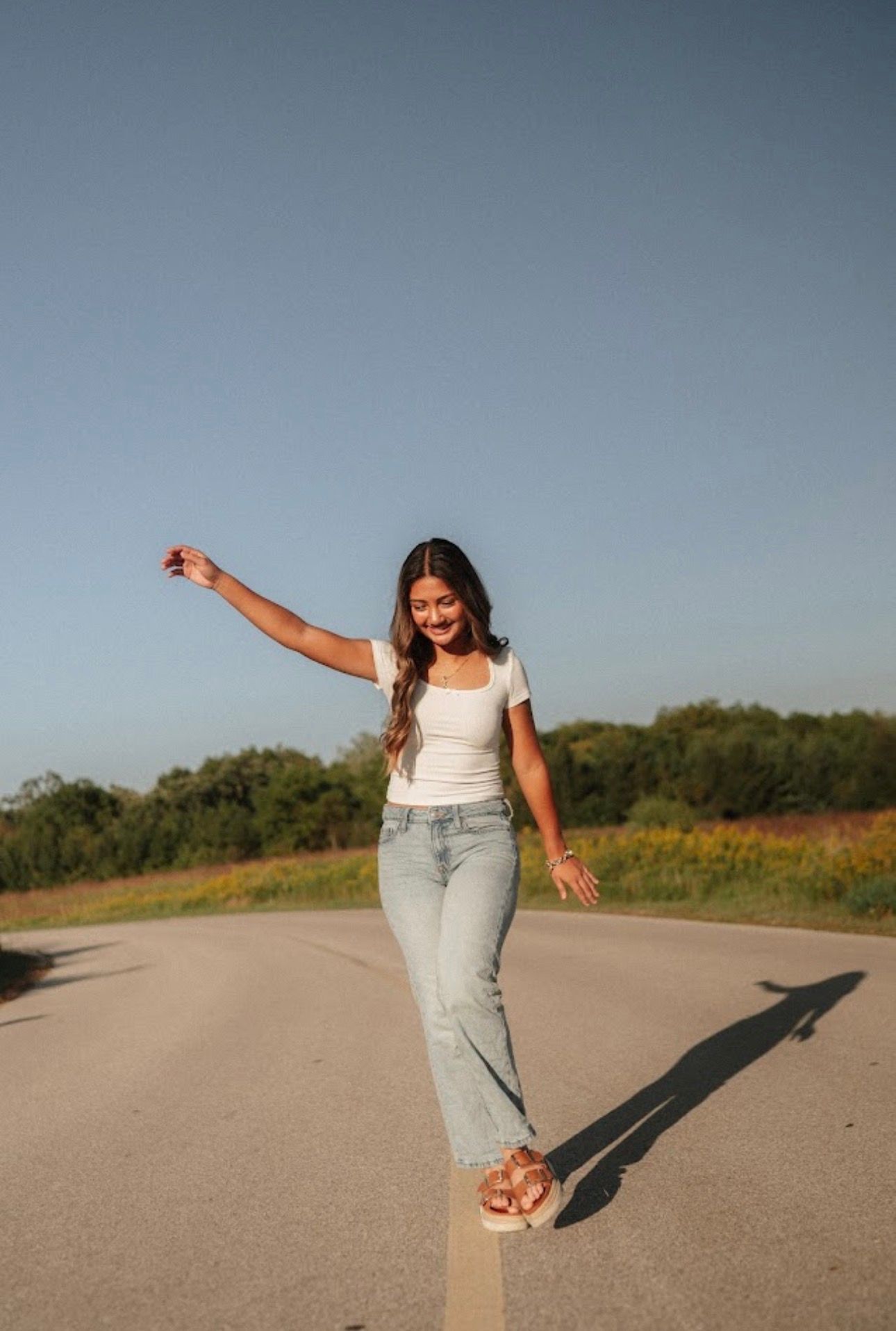 Someone walking joyfully down an empty road casting a long shadow in the late afternoon sun.