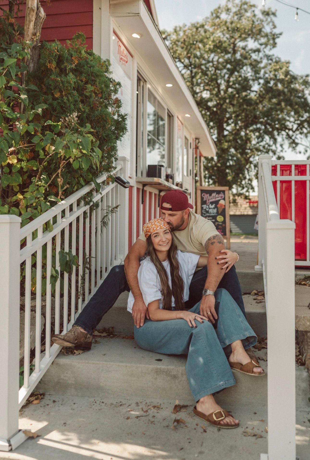 A casual portrait of people sitting on white porch steps of a red building.