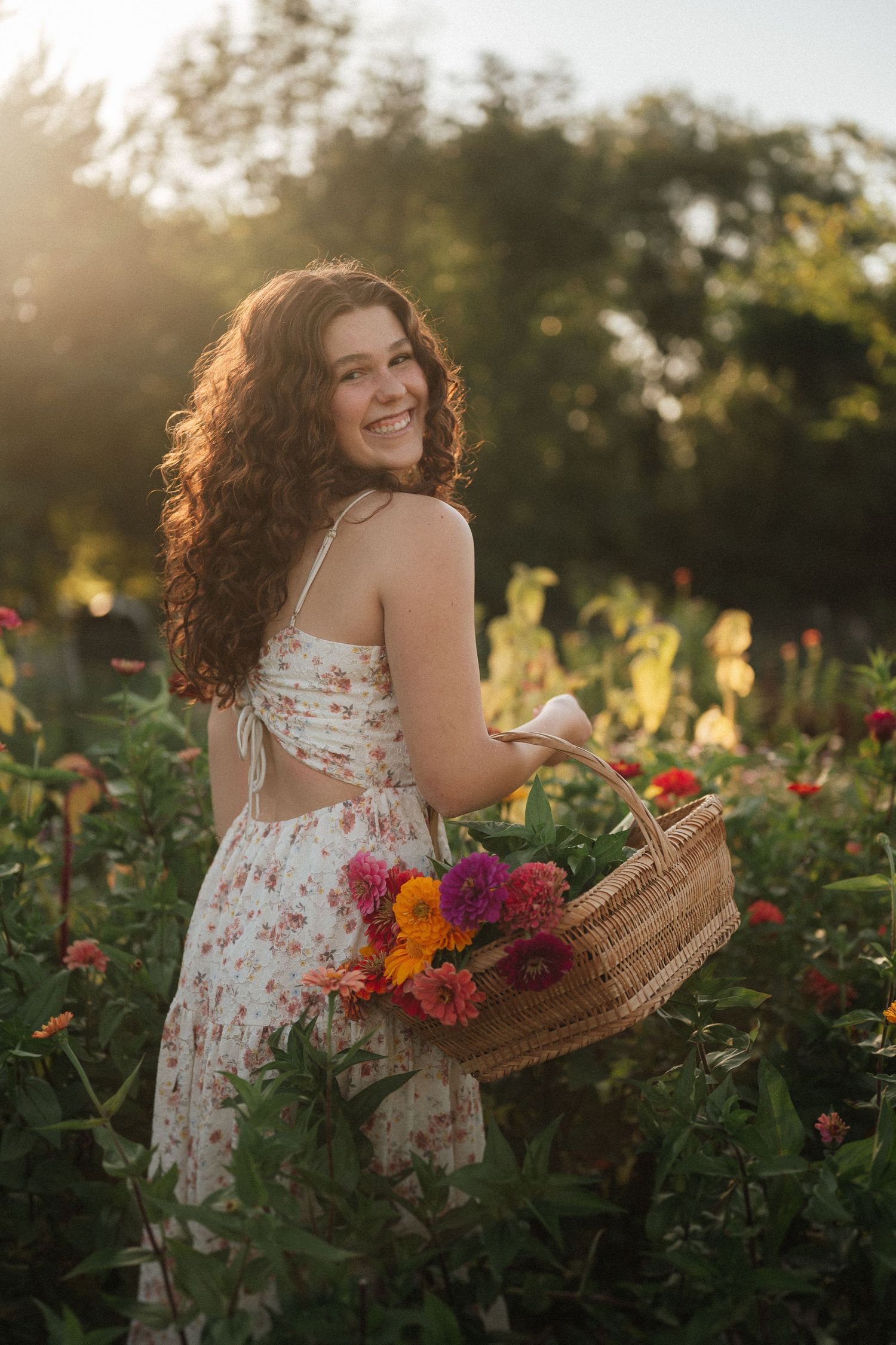 A floral sundress-clad figure holds a woven basket of colorful flowers in a garden during golden hour.