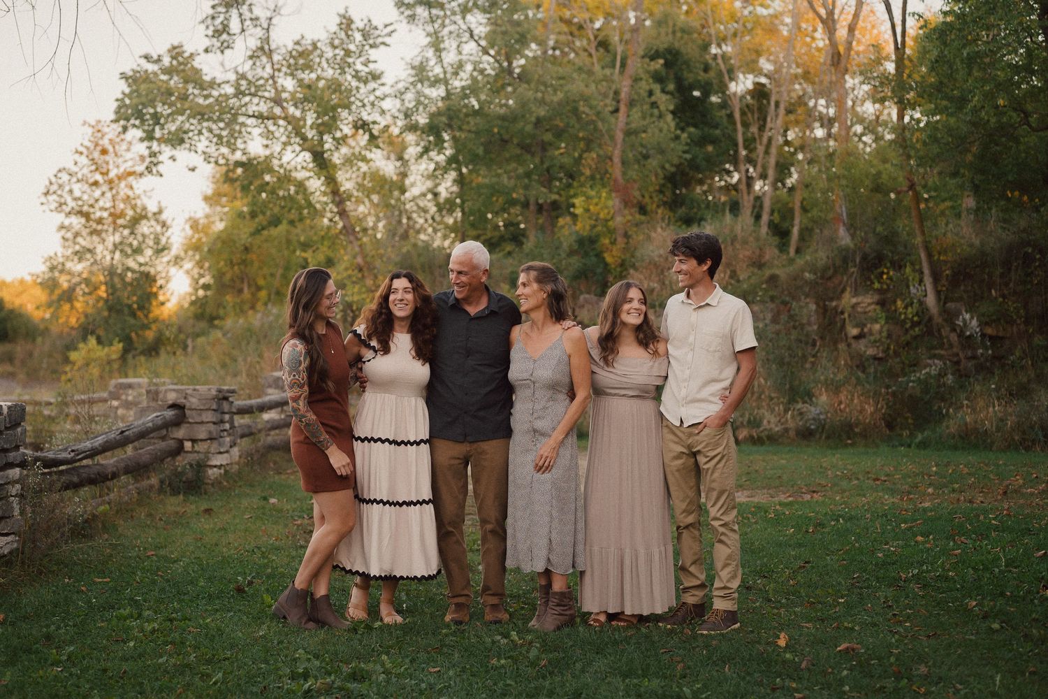 A group in coordinated neutral-toned outfits poses together outdoors during autumn at sunset.