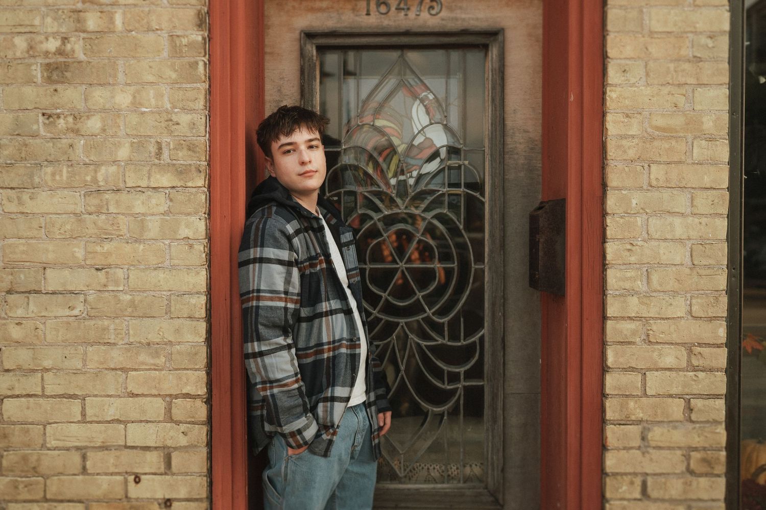 Someone leans against a brick wall with decorative windows and red trim in an architectural setting.