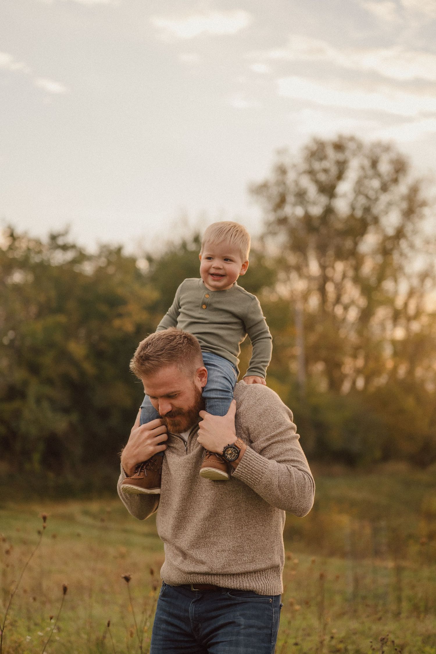 A joyful moment captured at sunset in a field as a parent carries a small child on their shoulders.